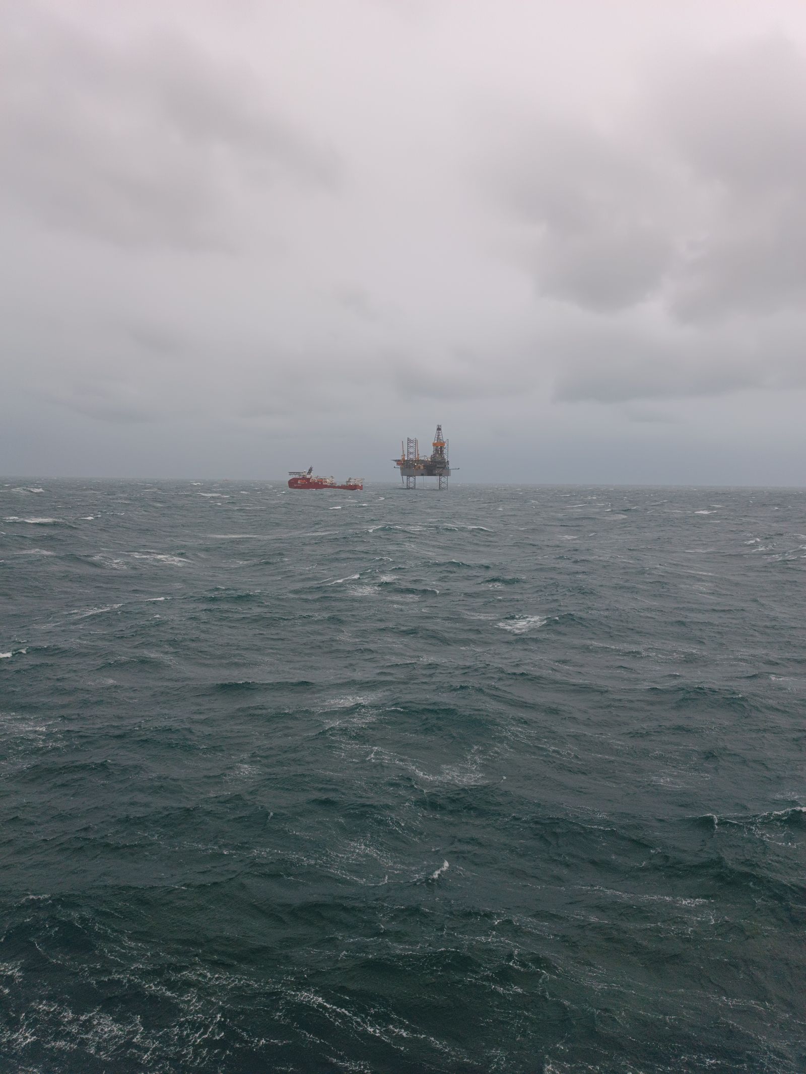 Support vessel and jack-up platform on the horizon under heavy sky